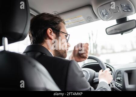 bearded bodyguard in occhiali da sole e auricolari di sicurezza che parlano durante la guida automobile moderna Foto Stock