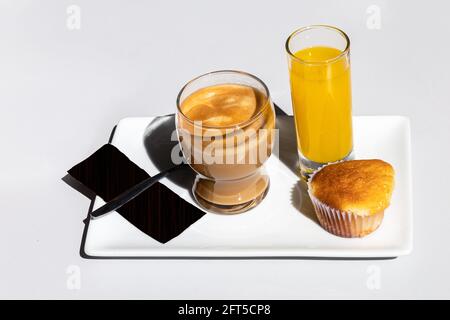 colazione continentale con caffè in un bicchiere con succo d'arancia e un muffin di pasticceria su un vassoio con fondo bianco e spazio di copia Foto Stock