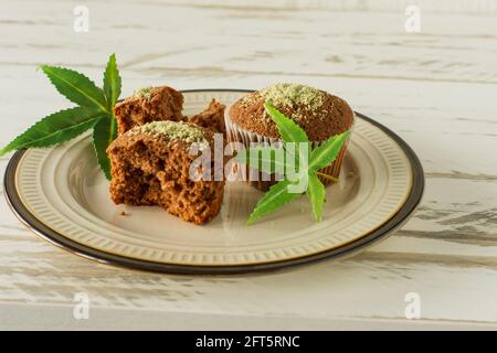 Muffin sani e gustosi privi di glutine e vegani in fila con semi di canapa su un tavolo di marmo. Muffin alla tazza di marijuana con foglie di cannabis. Foto Stock