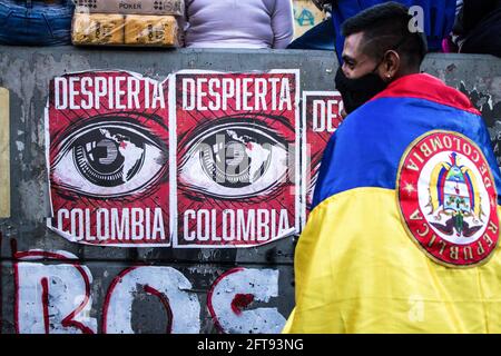 Un manifestante avvolto da una bandiera colombiana si trova accanto a manifesti che dicono che la Colombia si sveglia durante la dimostrazione.Plaza de Los Heroes (Piazza degli Eroi) a Bogotà, è stato uno dei 40 punti di dimostrazione durante lo sciopero nazionale DEGLI ANNI 19M. Al ventiduesimo giorno di protesta hanno preso parte in totale quindici mila persone. Le proteste in diverse parti del paese hanno cominciato a opporsi alla riforma fiscale. La polizia ha risposto con estrema violenza, e le richieste si sono moltiplicate man mano che la crisi economica si acuì. Credit: SOPA Images Limited/Alamy Live News Foto Stock