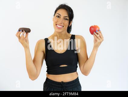 Giovane donna ispanica che tiene mela e ciambelle sorridendo con un sorriso felice e fresco sul viso. Mostrando i denti. Foto Stock