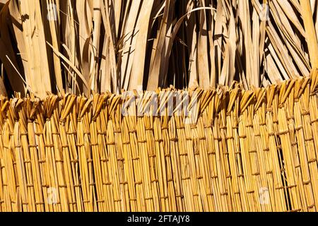 Tessuto di paglia con foglie di palma essiccate su sfondo. Tappeto tessuto fatto a mano. Flaxen tessitura maglia gialla immagine ravvicinata. Foto Stock