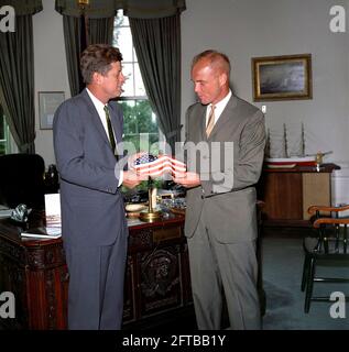 Il presidente John F. Kennedy riceve un dono di una bandiera americana dall'astronauta tenente colonnello John H. Glenn, Jr. (A destra); il Lt. Colon ha portato la bandiera nella sua tuta spaziale durante il suo volo orbitale a bordo del Mercury-Atlas 6, noto anche come amicizia 7. Sullo sfondo c'è l'assistente speciale del presidente, Kenneth P. o'Donnell. Ufficio ovale, Casa Bianca, Washington, D.C. Foto Stock