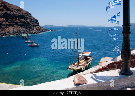 Barche da pesca sulle acque turchesi limpide del Mar Egeo presso il vecchio porto di Amoudi del villaggio di Oia sull'isola di Santorini, Grecia. E t Foto Stock