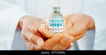 un operatore sanitario, in un camice bianco da laboratorio, con una fiala vaccinale covid-19 simulata nelle mani, in un formato panoramico da utilizzare come banner web o heade Foto Stock