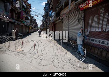 Srinagar, India. 21 Maggio 2021. La gente cammina oltre le barricate lungo la strada durante le restrizioni Lal chowk.The autorità su Venerdì stretto il coprifuoco Covid-19 nel distretto di Srinagar alla vigilia del anniversario della morte di Mirwaiz Molvi Mohammad Farooq e Abdul Ghani Lone, che è stato segnato il 21 maggio a Kashmir. Credit: SOPA Images Limited/Alamy Live News Foto Stock