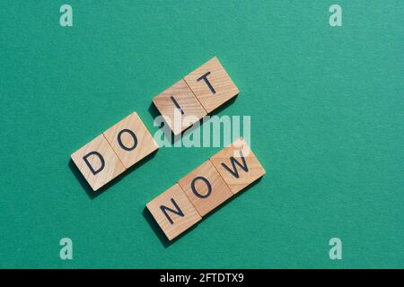 Fate ora, parole motivazionali in lettere alfabetiche in legno isolate su sfondo verde con spazio di copia Foto Stock