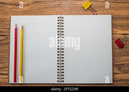 Notebook con foglio bianco aperto sul tavolo, accanto ai materiali di consumo rosso e giallo: Matite e clip per rilegatori Foto Stock