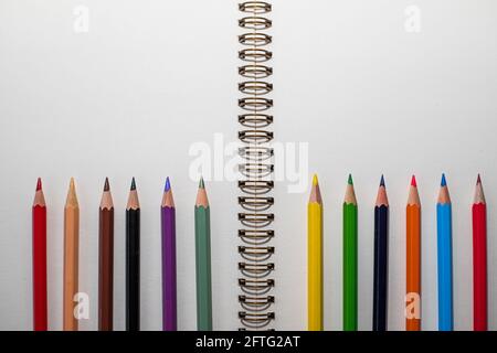 Foto macro: Apri il notebook con i fogli bianchi sul tavolo e un sacco di matite colorate allineate in basso Foto Stock