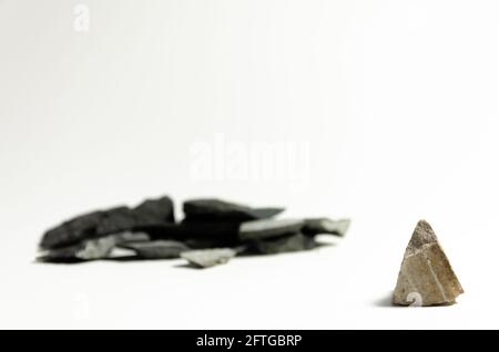 Una roccia isolata si erge da sola di fronte ad un gruppo di diverse rocce osservanti su uno sfondo bianco Foto Stock