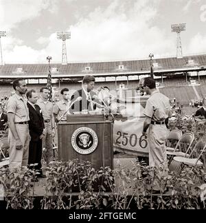 Il presidente John F. Kennedy riceve la bandiera della 2506a Brigata dell'invasione cubana dai membri della brigata durante una cerimonia di presentazione all'Orange Bowl Stadium di Miami, Florida. Sulla piattaforma dei relatori (da sinistra a destra): Erneido Oliva, secondo al comando della brigata; Sindaco di Miami, Robert King High; Jose Pérez San Román, comandante della brigata; Manuel Artime, capo civile della brigata; Presidente Kennedy (al leggio, con bandiera); Interprete del Dipartimento di Stato degli Stati Uniti, Donald Barnes (per lo più nascosto dietro la bandiera); First Lady Jacqueline Kennedy-parzialmente nascosto dietro la bandiera. Foto Stock