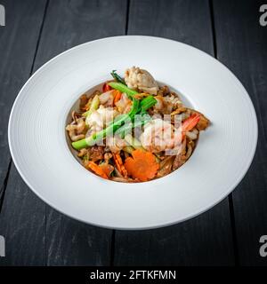 Un piatto di Thai Pad vedere EW Noodle con frutti di mare E verdure su sfondo di legno nero Foto Stock