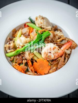 Un piatto di Thai Pad vedere EW Noodle con frutti di mare E verdure su sfondo di legno nero Foto Stock