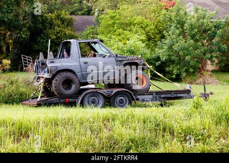 Loxahatchee, Florida, USA - 16 maggio 2021: Autocarro a trazione integrale con pneumatici enormi di terra jumbo su un rimorchio di motoscafo arrugginito, parafanghi mancanti. Foto Stock