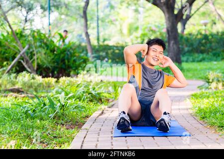 Uomo asiatico facendo sgranocchia per six pack formazione nel parco Foto Stock