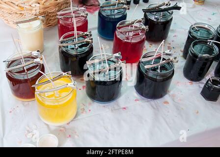 Fare barattolo candele di cera di soia questi barattoli con clip di metallo stanno tenendo doppio pulcini in vari colori di cera liquida su questa panca di candlemakers. CH Foto Stock