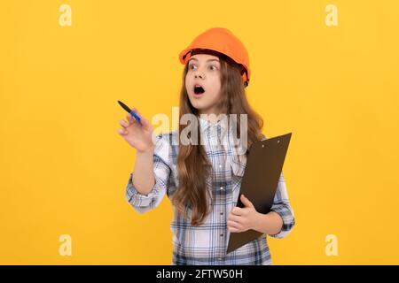 scioccata ragazza teen in casco e camicia a scacchi facendo appunti sulla clipboard, lavorando Foto Stock