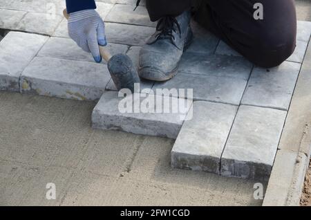 Costruzione di pavimentazione vicino alla casa. Lo strato di mattoni posiziona blocchi di pietra per pavimentazione in calcestruzzo per la costruzione di un marciapiede Foto Stock