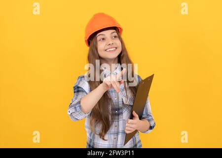 felice ragazza teenager in casco e camicia a scacchi facendo note sulla clipboard, occupato Foto Stock