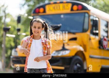 Bambina in piedi da una grande porta dell'autobus della scuola con il suo zaino. Foto Stock