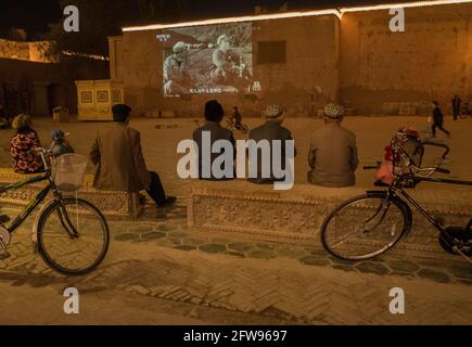 Uyhgur uomini seduti in una piccola piazza guardando un film di propaganda della Rivoluzione cinese. Kashgar, Repubblica popolare cinese 2019 Foto Stock