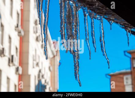 Ghiacciate contro il cielo blu. Ghiaccio trasparente chiaro che brilla al sole in inverno o in primavera. Acqua surgelata sotto forma di cono lungo e ghiacciato. Foto Stock