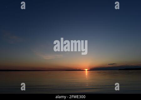 Fascio di sole al tramonto dalle nuvole all'orizzonte sopra il lago d'acqua Foto Stock