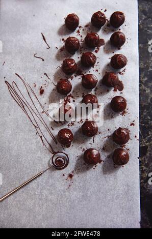 Vista dall'alto della composizione con tartufi al cioccolato e utensili al cioccolato cosparso di cacao in polvere su carta da forno bianca pergamena Foto Stock