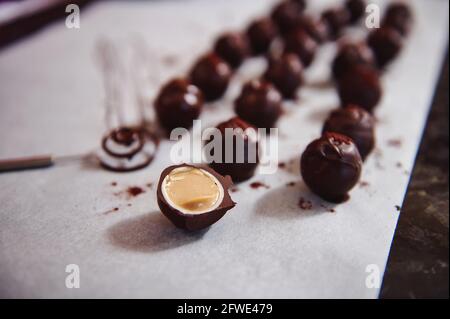 Tartufi di cioccolato su carta pergamena e accento in primo piano con caramelle di cioccolato tagliate a metà e farcite con caramello salato. Foto Stock
