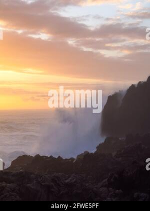 Tramonto con grandi onde che si infrangono in modo spettacolare contro alte scogliere rocciose aride lungo la costa di Tsitsikamma in Sud Africa, Foto Stock