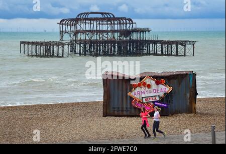 Brighton UK 22 maggio 2021 - i corridori passano dal vecchio contenitore di spedizione che è comparso sulla spiaggia di Brighton per promuovere il nuovo film di Netflix 'Army of the Dead' su una mattina soda inSeasonably fredda lungo la costa meridionale : Credit Simon Dack / Alamy Live News Foto Stock