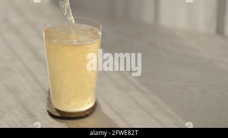 l'uomo versa la birra allo zenzero dalla bottiglia di vetro in bicchiere sul tavolo di quercia bianca con luce del tramonto, foto ampia Foto Stock