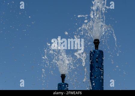 Due sprinkler blu per il parco acquatico che spruzzano acqua sopra per il divertimento estivo dei bambini. Foto Stock