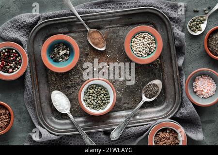 Varie spezie in cucchiai orientali in ceramica e coppe da pizzico su vassoio di metallo vintage scuro. Asciugamano in tessuto su sfondo testurizzato. Disposizione piatta, vista dall'alto Foto Stock