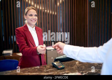 giovane addetta alla reception sorridendo ad un ospite, restituendogli la carta di credito Foto Stock