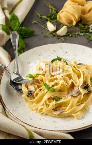 Fettuccine di pasta con funghi e prosciutto di pollo fritto in cremoso salsa di formaggio su uno sfondo di legno chiaro Foto Stock