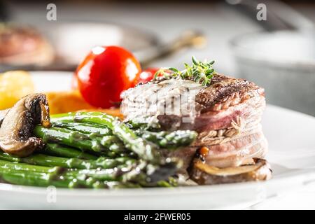 Bistecca alla griglia con pancetta servita su un piatto con asparagi, funghi e pomodoro. Foto Stock