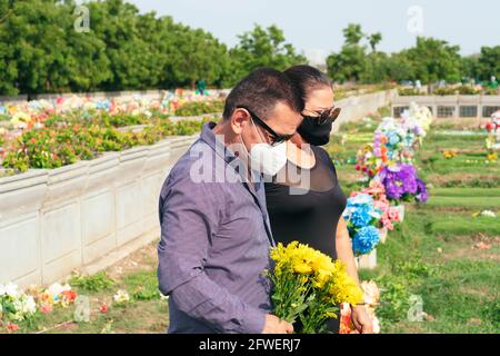 Coppia nel cimitero lutto che tiene in mano fiori gialli Foto Stock