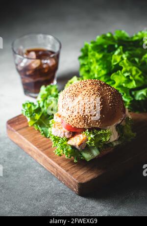 Delizioso hamburger di salmone, servito su tavola di legno. Fishburger con insalata fresca, verdure fresche e salsa. Hamburger di pesce sano croccante. Messa a fuoco selettiva Foto Stock