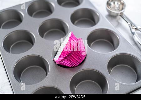 Cottura di cupcake al cioccolato. Fodera teglia per cupcake in metallo con fodere per cupcake. Foto Stock