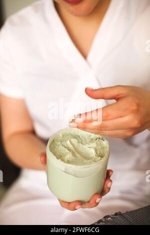 Alto angolo di raccolto anonimo cosmetologa femminile con vaso di crema verde nutriente nel salone di bellezza Foto Stock