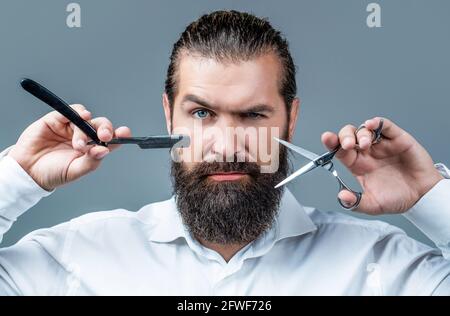 Ragazzo brutale, forbici, rasoio dritto. Cliente bearded che visita il barbiere. Forbici da barbiere e rasoio dritto, barbiere, tuta. Barbiere d'epoca Foto Stock