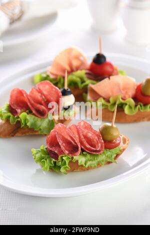 Tartine di baguette tenue con lattuga, salame o prosciutto di Parma, pomodori, mozzarella e olive. Piatto assortito di prelibatezze per la festa. Foto Stock