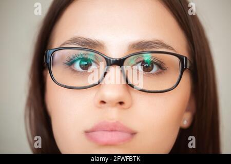 Closeup di raccolto giovane femmina di brunette con gli occhi marroni e. in occhiali su sfondo grigio Foto Stock