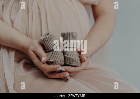 La madre in attesa si prepara per dare alla luce il bambino tiene gli stivali in mani pone indoor essere sul terzo trimestre Foto Stock