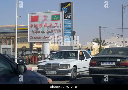 MAURITANIA, Nouakchott, Corona Pandemic, cartellone per il vaccino COVID-19 cinese CoronaVac della società farmaceutica cinese Sinovac Biotech, tzraffic, vecchie auto usate importate dall'Europa, auto tedesca Mercedes-Benz Foto Stock