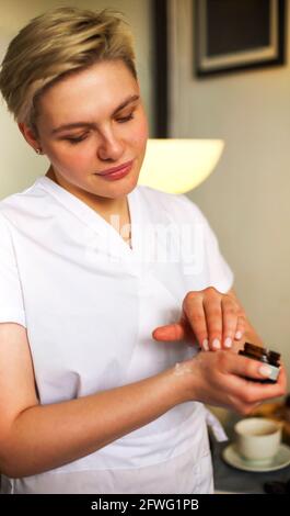 Giovane beautician donna che applica la crema dal vaso a mano prima procedura in salone Foto Stock