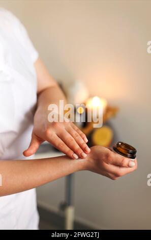 Giovane beautician donna che applica la crema dal vaso a mano prima procedura in salone Foto Stock
