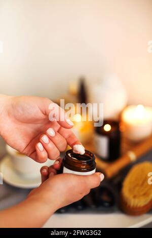 Giovane beautician donna che applica la crema dal vaso a mano prima procedura in salone Foto Stock