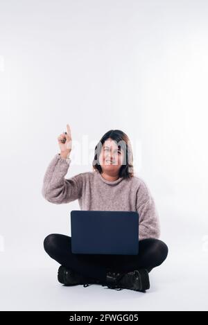 La donna con un computer portatile seduto sul pavimento è rivolta verso l'alto con l'addebito su sfondo bianco. Concetto di shopping. Spazio di copia Foto Stock